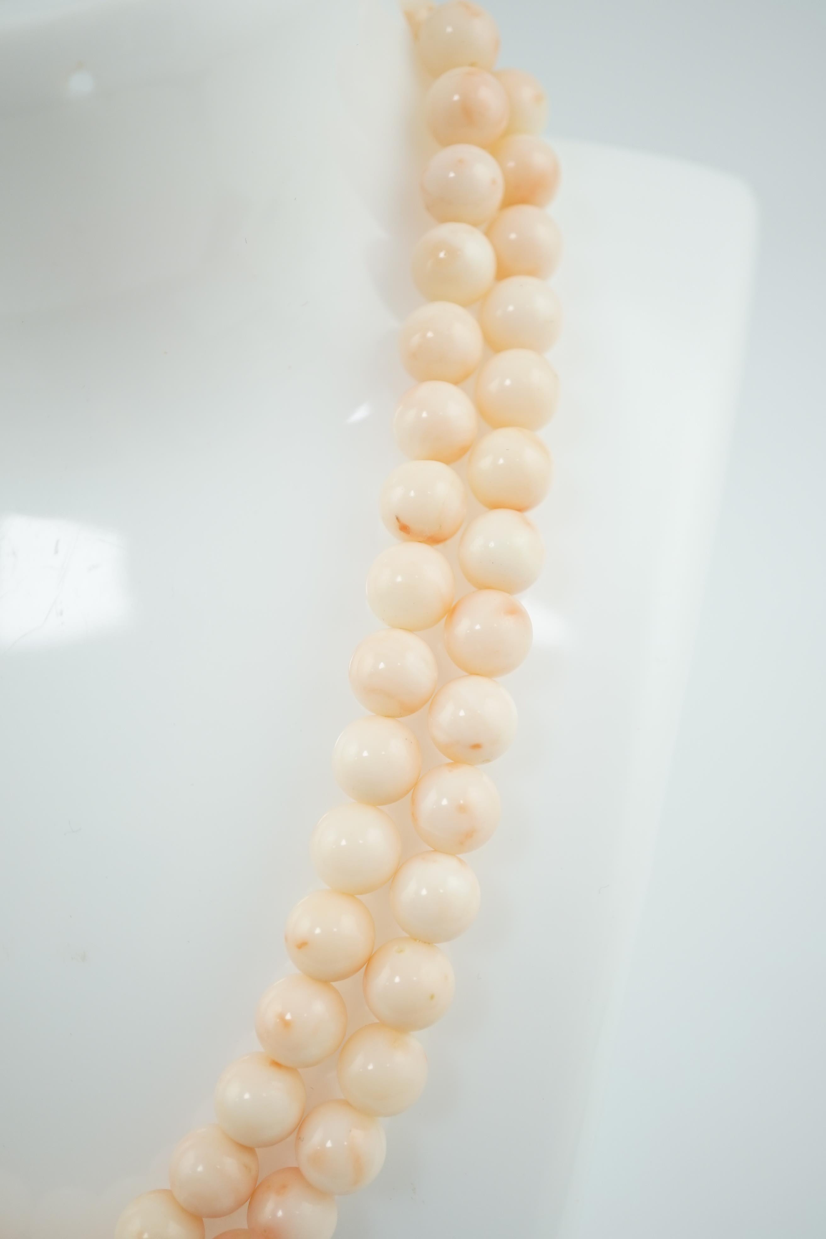 A double strand pale pink coral bead choker necklace, with round and baguette cut diamond cluster set bow shaped 18k white gold clasp
